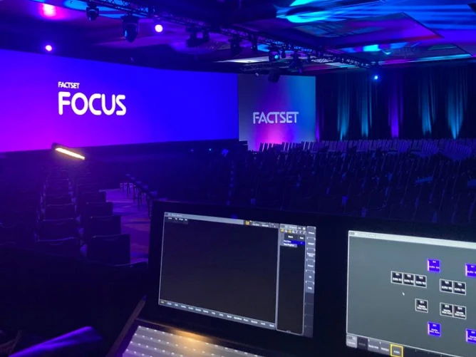 Panoramic curved LED video wall wrapping three sides of a hotel ballroom stage, displaying a multi-colored test-pattern grid of red, green, blue, cyan, magenta, and yellow bars for pixel calibration, under a flown truss lighting grid and crystal chandelier
