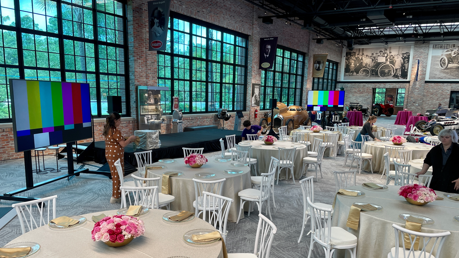 Two 90" monitors at event Live production control room with five operators wearing headsets seated at desks loaded with laptops, video switchers, and audio mixers; two large wall-mounted screens display multi-view camera feeds and a bright studio preview in a carpeted office space